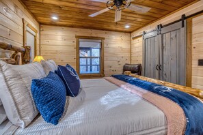 A log cabin bedroom with a bed, pillows, a window, and a ceiling fan. - Stunning Mountain Views - Hot Tub + EV Charger! (Mineral Bluff)