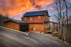 A two-story log cabin with a garage and a covered porch. - Stunning Mountain Views - Hot Tub + EV Charger! (Mineral Bluff)