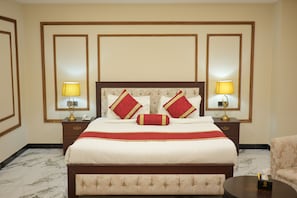 Ein Hotelzimmer mit einem großen Bett, zwei Nachttischen mit Lampen, einer Kopfstütze mit dekorativen Kissen und einem marmorbodenbelagten Boden.