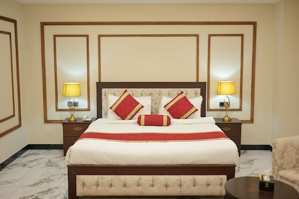 A hotel room with a large bed, two bedside tables with lamps, a headboard with decorative pillows, and a marble-tiled floor.