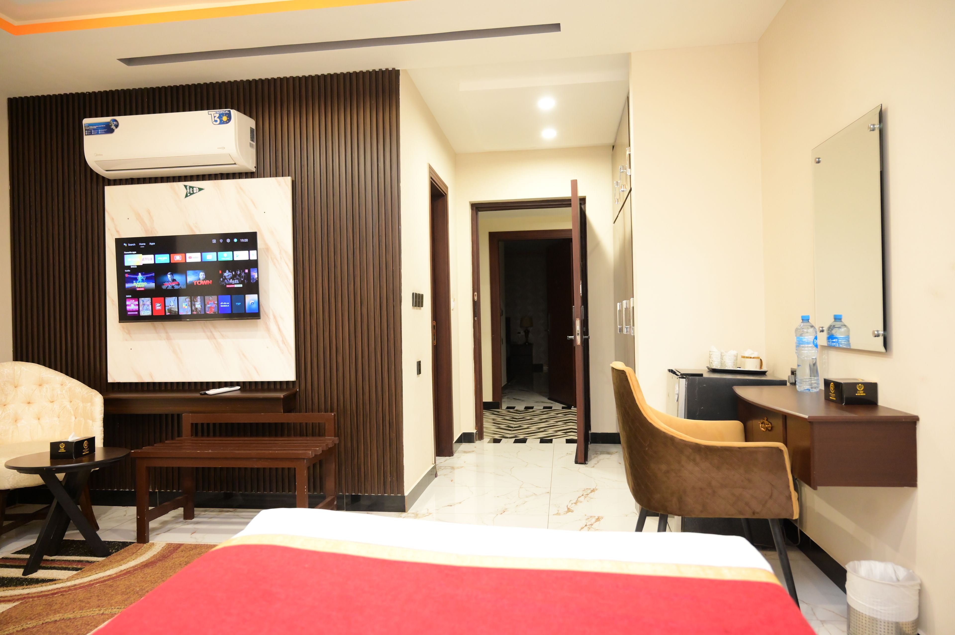 A hotel room with a bed, a TV mounted on the wall, a desk with a chair, and a bathroom visible through an open door.