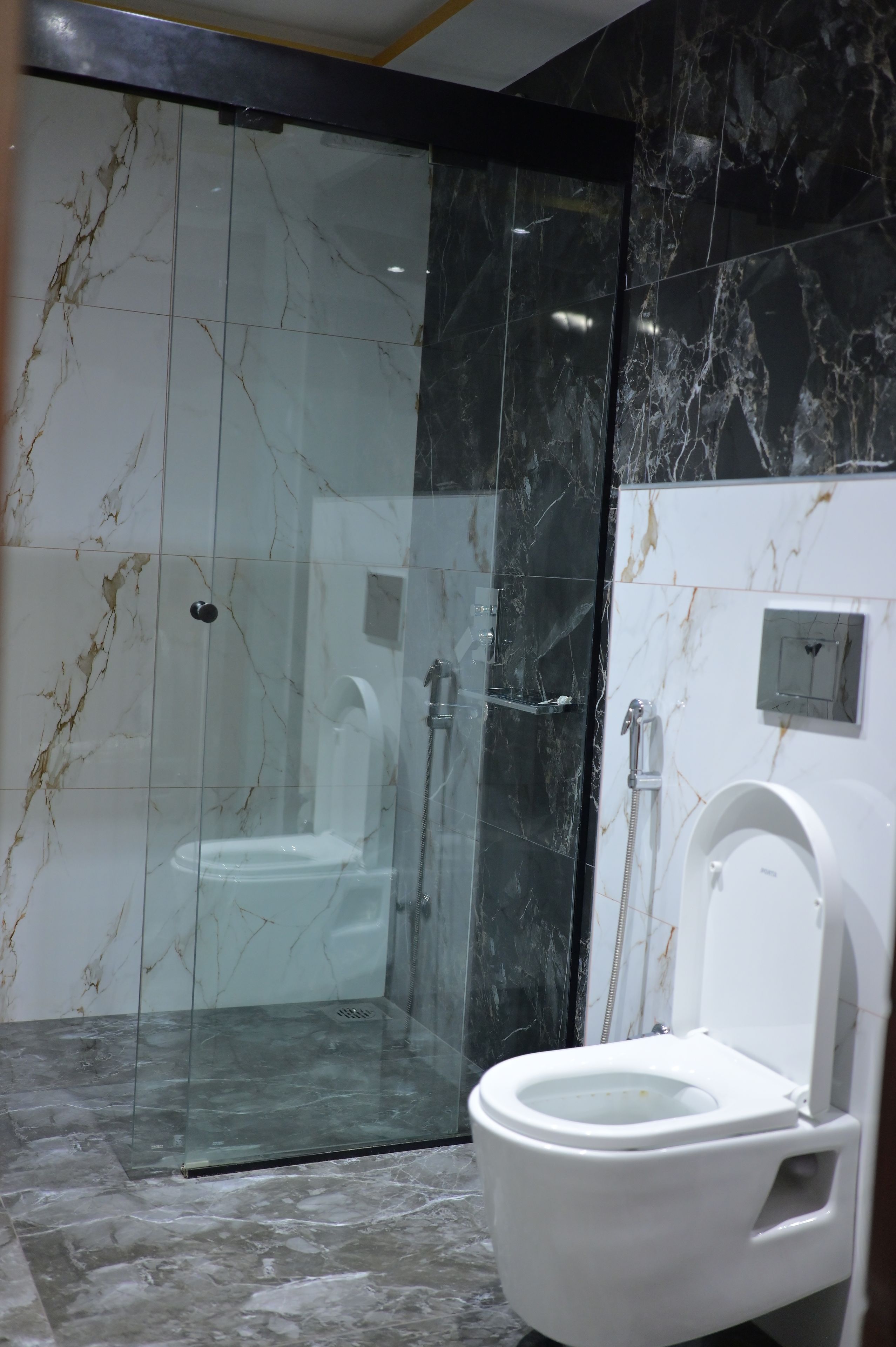 Un baño moderno con ducha envuelta en vidrio, inodoro y paredes de mármol.