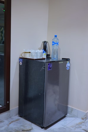 A compact refrigerator with a water bottle and a coffee maker on top, placed against a wall with a tiled floor.