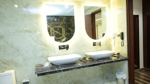 Un baño con dos lavamanos, un espejo, un teléfono y un cubo de basura.