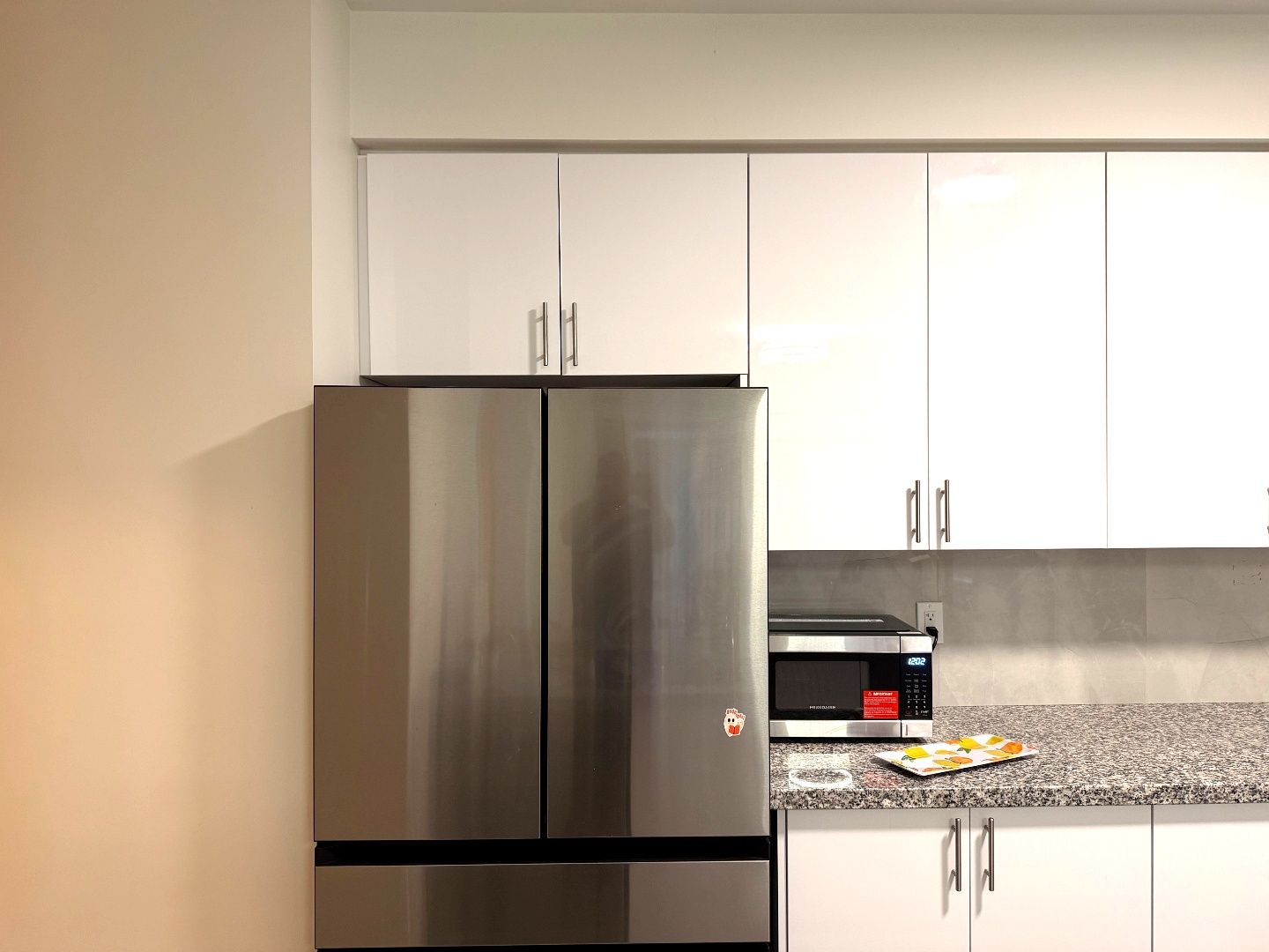 A kitchen with a stainless steel refrigerator, a microwave, and a granite countertop.