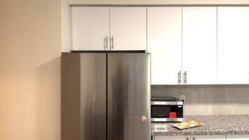 A kitchen with a stainless steel refrigerator, a microwave, and a granite countertop.