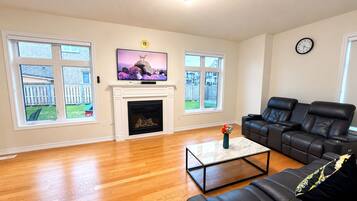 A living room with a fireplace, a television, a sofa, and large windows.