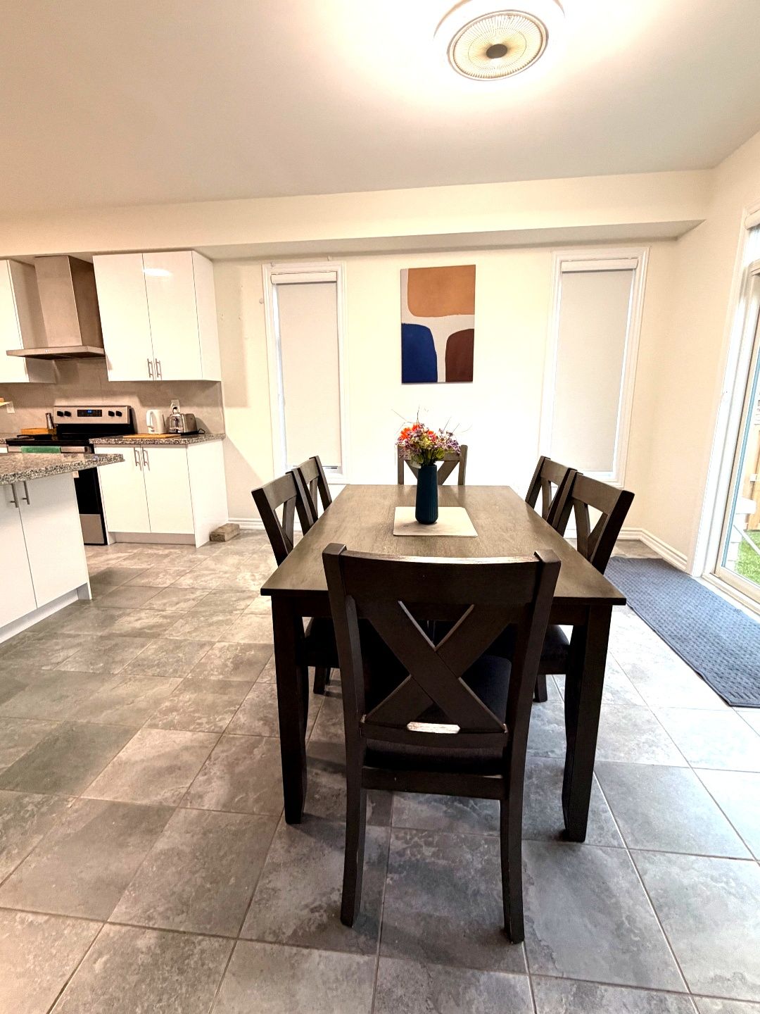 A modern kitchen with white cabinets, a dining table with six chairs, and a decorative vase with flowers.