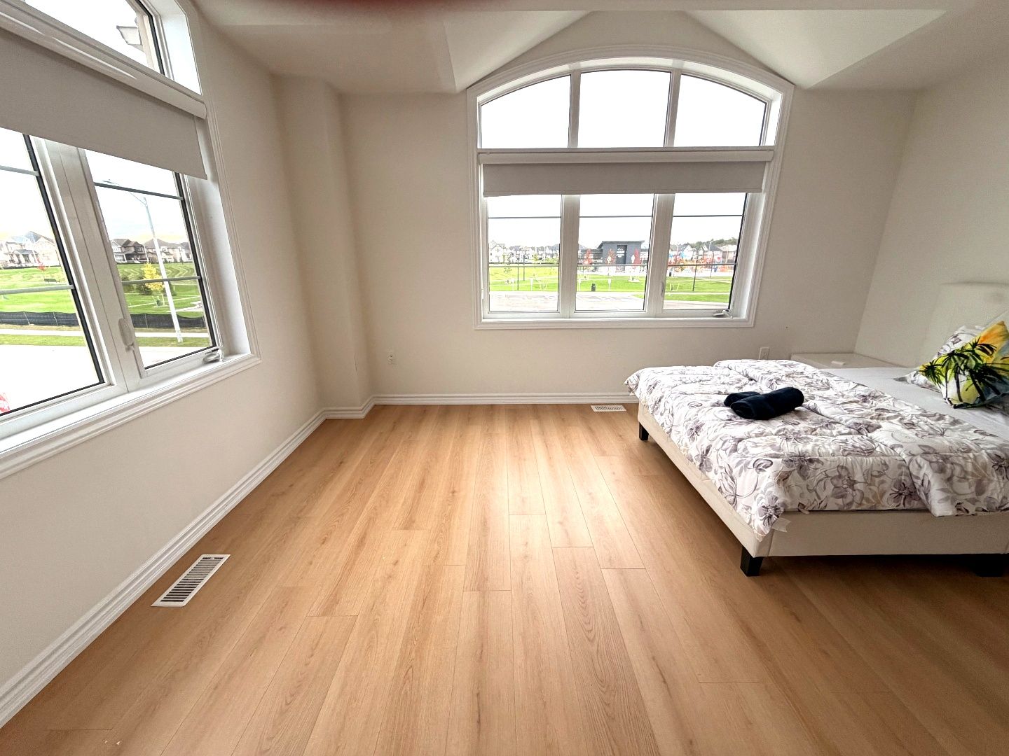 A bedroom with a large window, wooden flooring, and a bed with a floral bedspread.