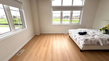 A bedroom with a large window, wooden flooring, and a bed with a floral bedspread.