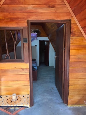 A wooden cabin with a sloped roof, a small table with a cup, and a door leading to another room.