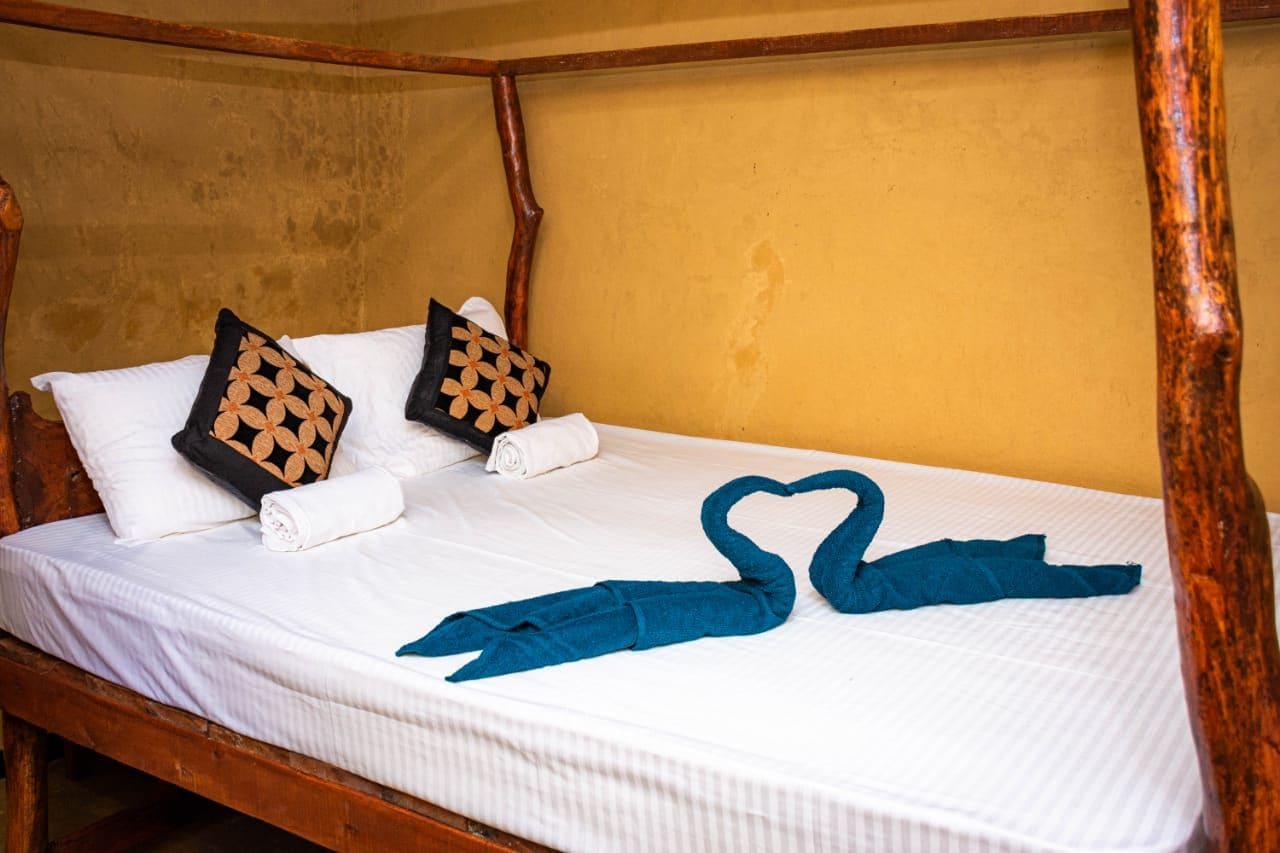 A bed with white linens, two decorative pillows, and a heart-shaped towel arrangement.
