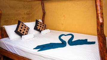 A bed with white linens, two decorative pillows, and a heart-shaped towel arrangement.