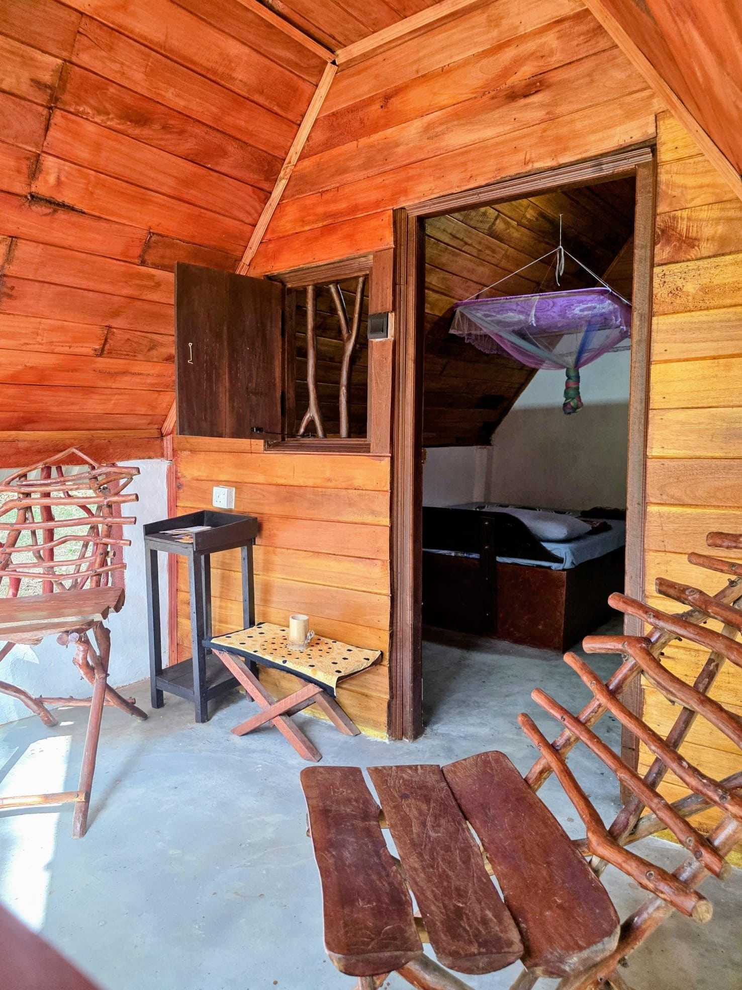 A wooden cabin interior with a bed, a table, and a bench.