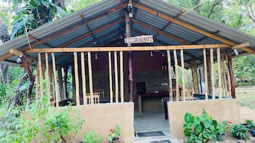 Un restaurante rústico al aire libre con techo de lámina corrugada, vigas de madera y un letrero que indica su función.