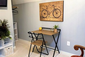 A compact room with a small wooden desk, two chairs, a potted plant, and a wall-mounted bicycle artwork.