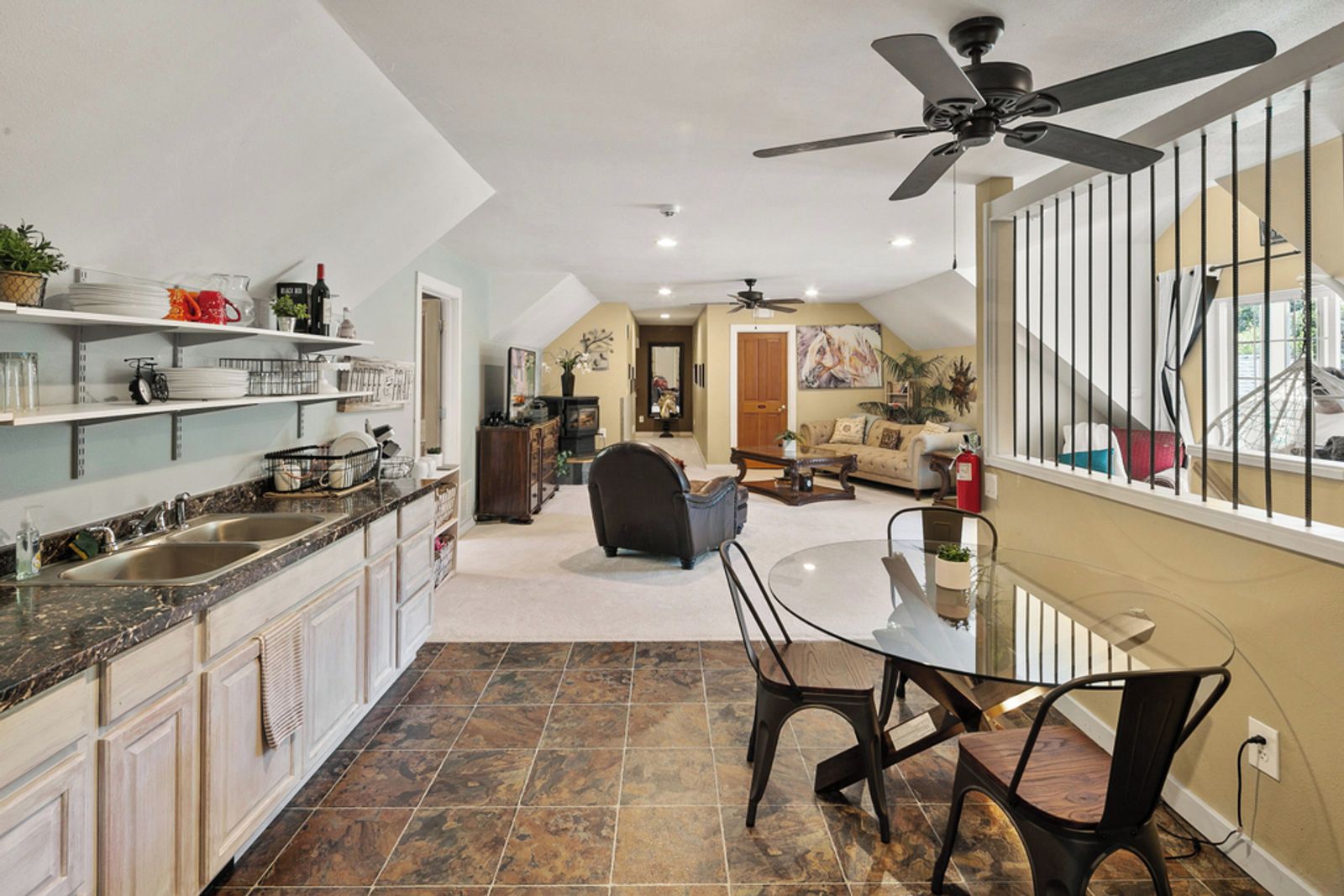 A modern kitchen with granite countertops, a dining area with a glass table, and a ceiling fan.