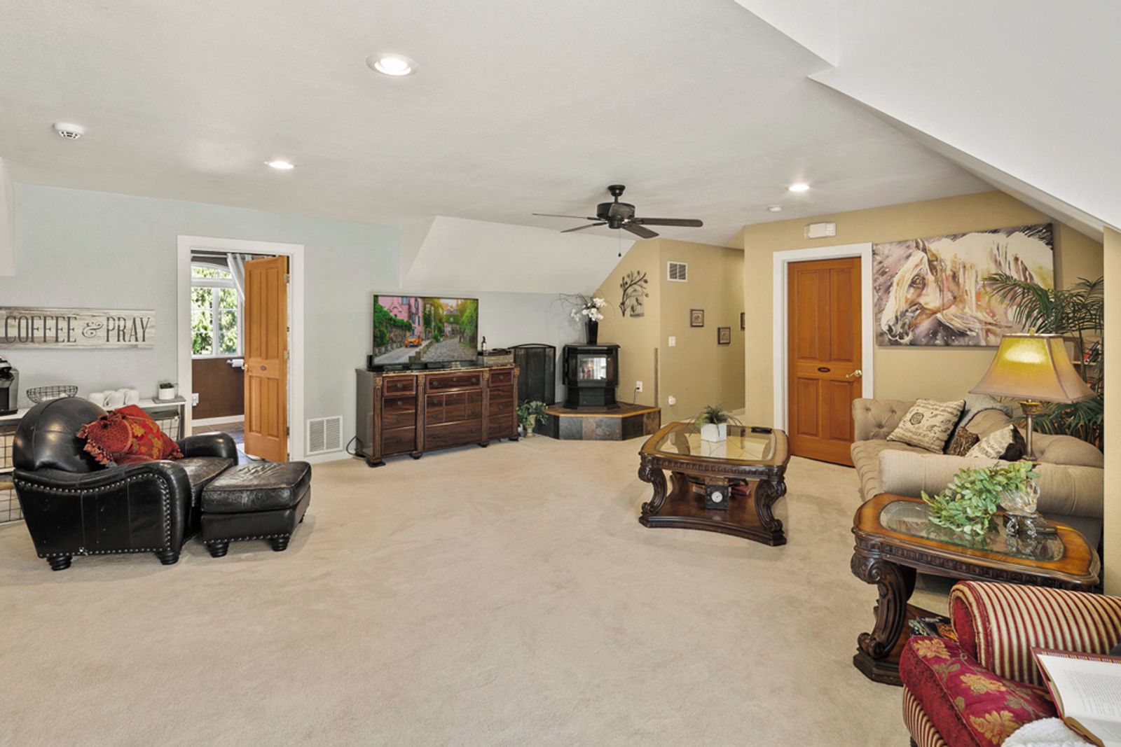 A spacious living room with a high ceiling, a ceiling fan, a television, a fireplace, and a comfortable seating area with a sofa and armchairs.