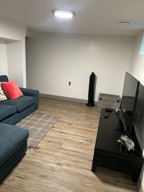 A modern living room with a blue sofa, a black entertainment unit, and a wooden floor. - Cozy basement nook in the heart of Edmonton. (Edmonton)