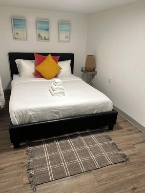 A neatly made bed with white bedding and a brown checkered rug in front. - Cozy basement nook in the heart of Edmonton. (Edmonton)