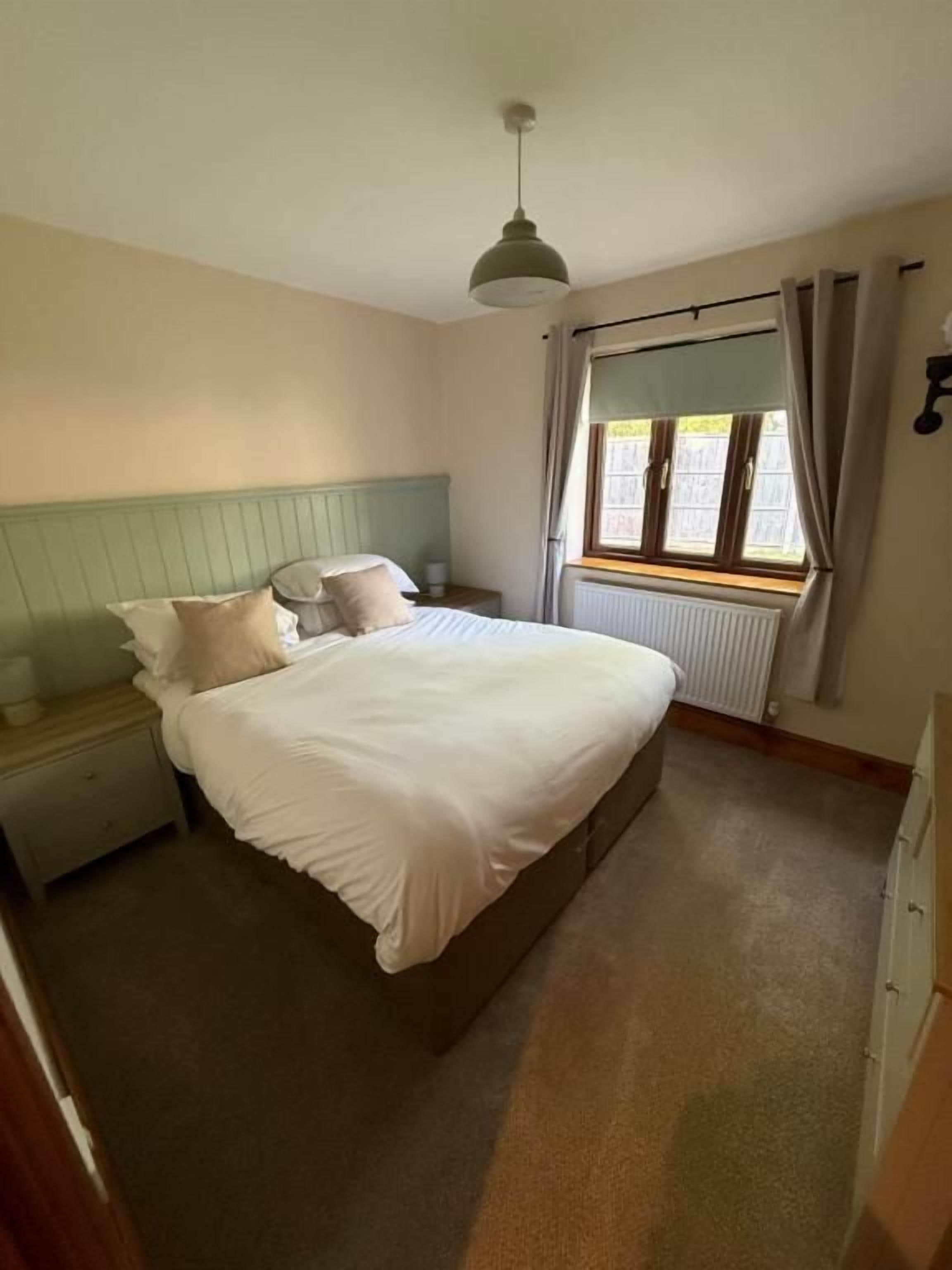 Un dormitorio con cama, mesita de noche, ventana y radiador.