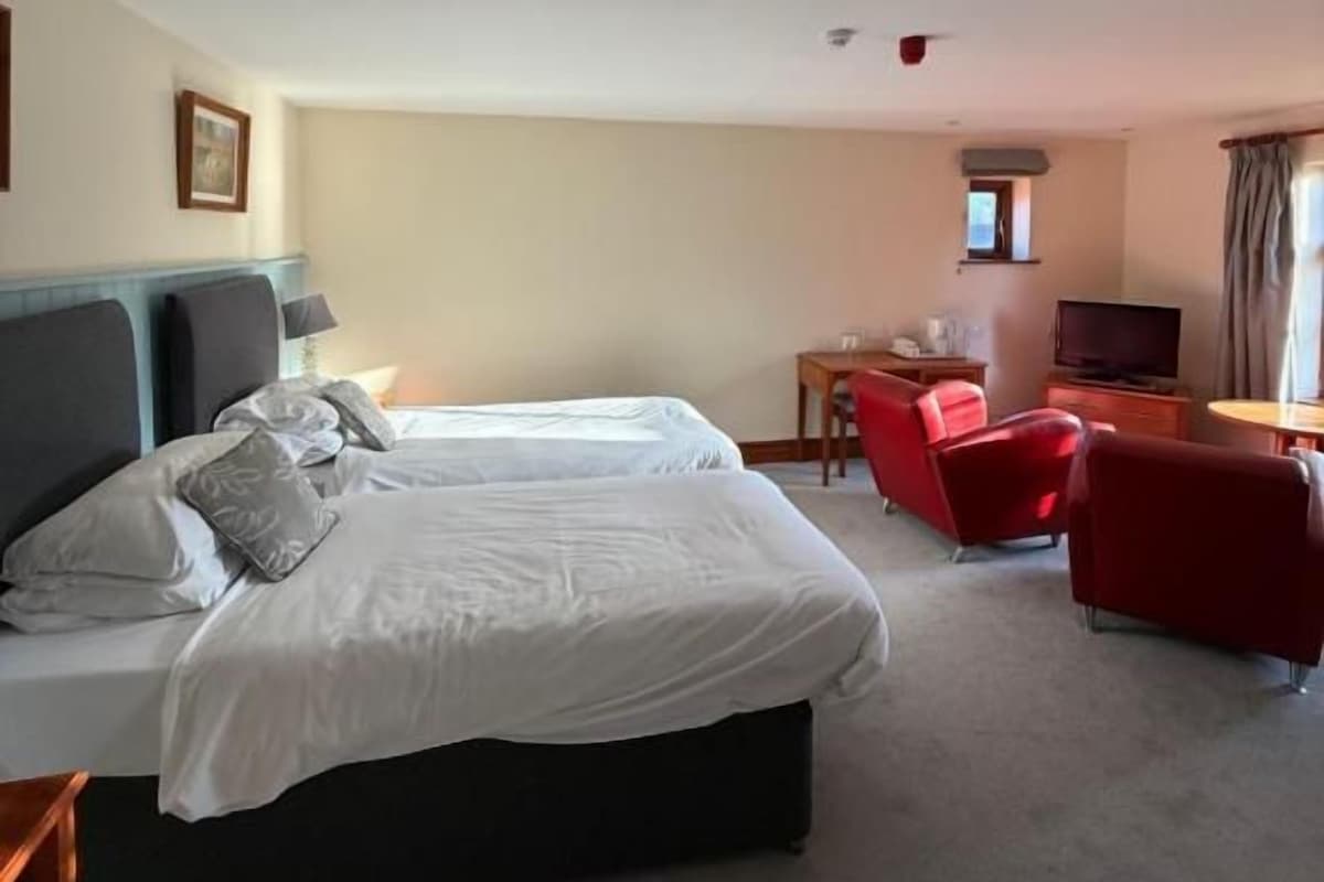 Una habitación de hotel con una cama, un escritorio, un televisor y dos sillas rojas.