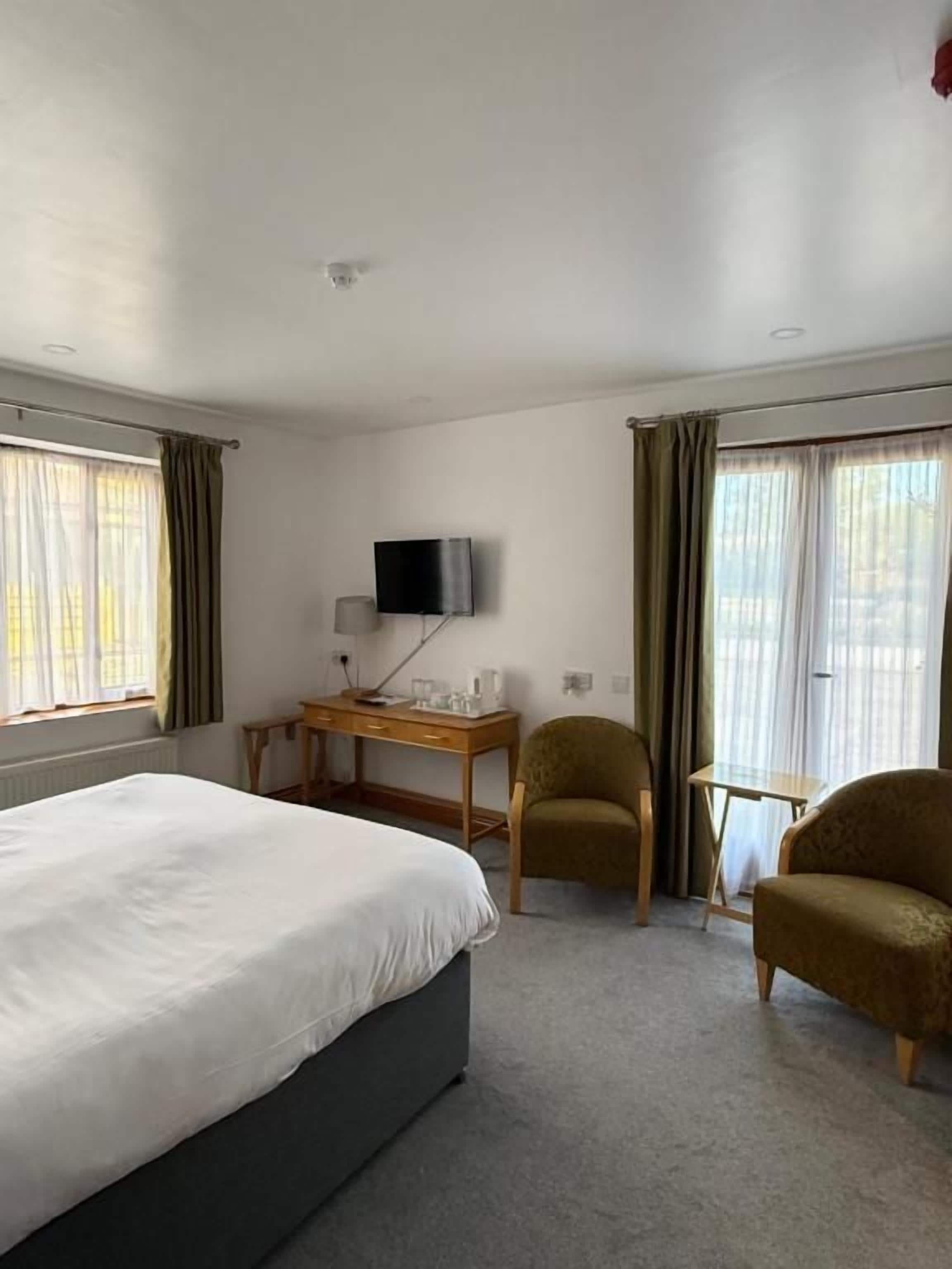 A hotel room with a bed, a desk with a TV, two chairs, and a window with curtains.