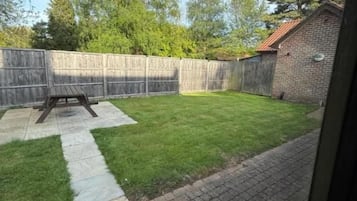 Un jardin avec une clôture en bois, une terrasse en briques et une pelouse verdoyante.