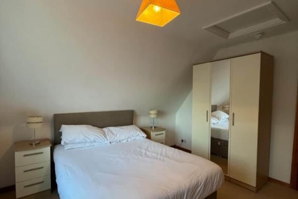 Un dormitorio con cama, mesitas de noche, armario y lámpara en el techo.