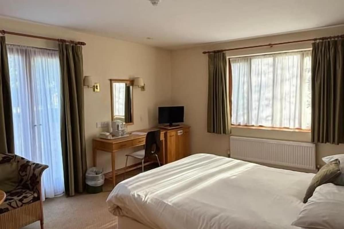 Habitación de hotel con cama, escritorio, silla, televisión y ventana con cortinas.