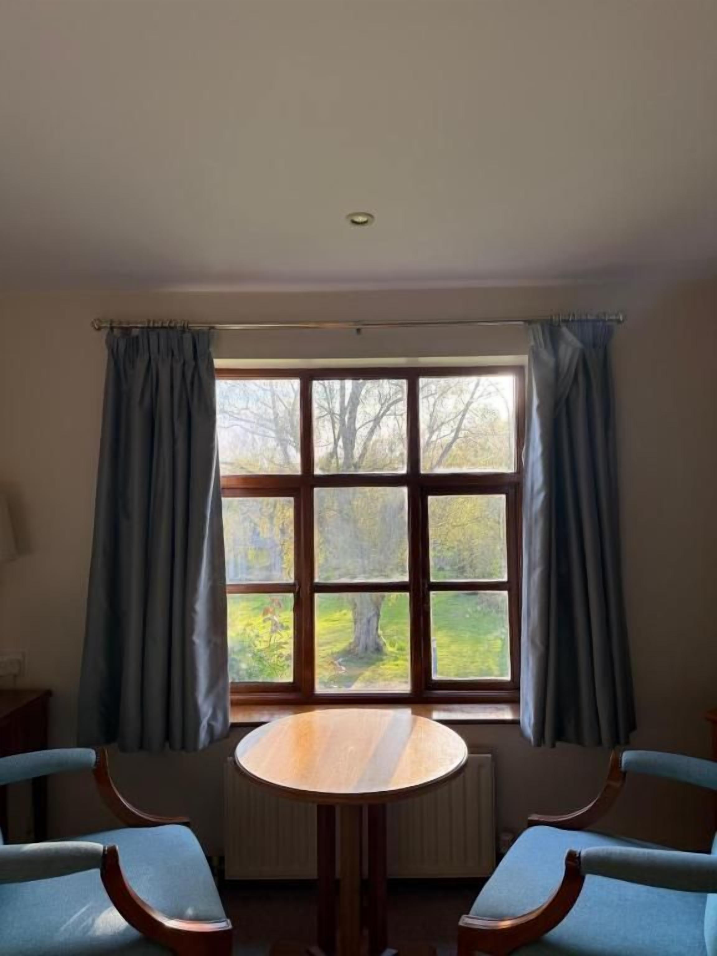 A room with a round table, two chairs, a window with curtains, and a radiator.