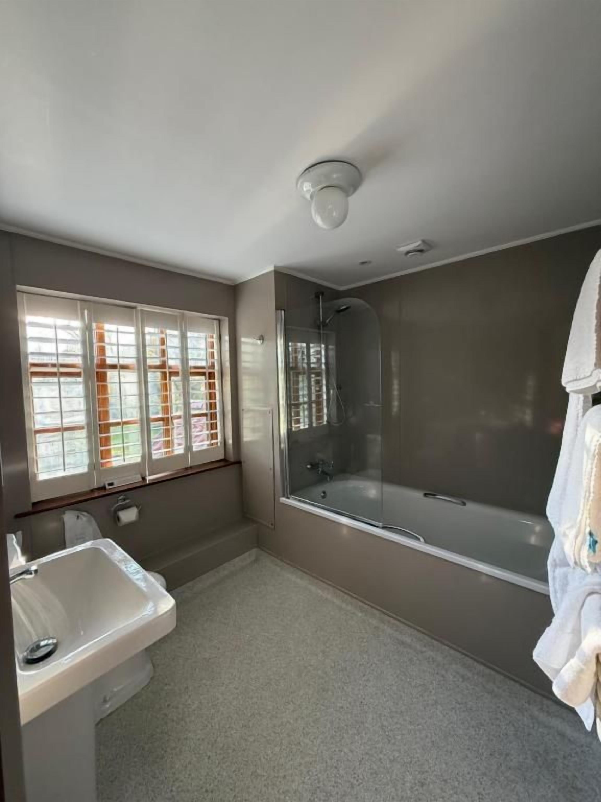 Un baño con bañera, lavamanos y ventana con persianas.