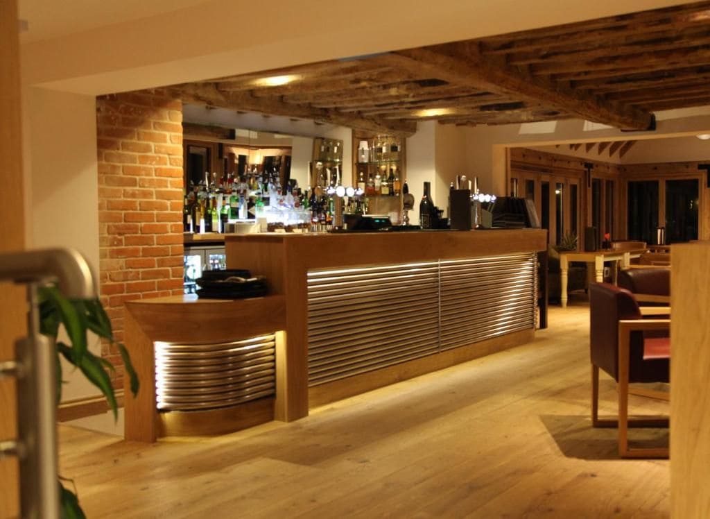 A bar area with a brick wall, wooden counter, and shelves of bottles.