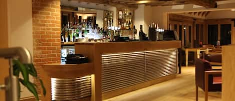 A bar area with a brick wall, wooden counter, and shelves of bottles.