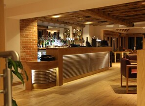 Zona de bar con pared de ladrillo, mostrador de madera y estanterías llenas de botellas.