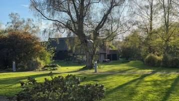 Un césped con un árbol grande, una casa y una construcción de piedra.