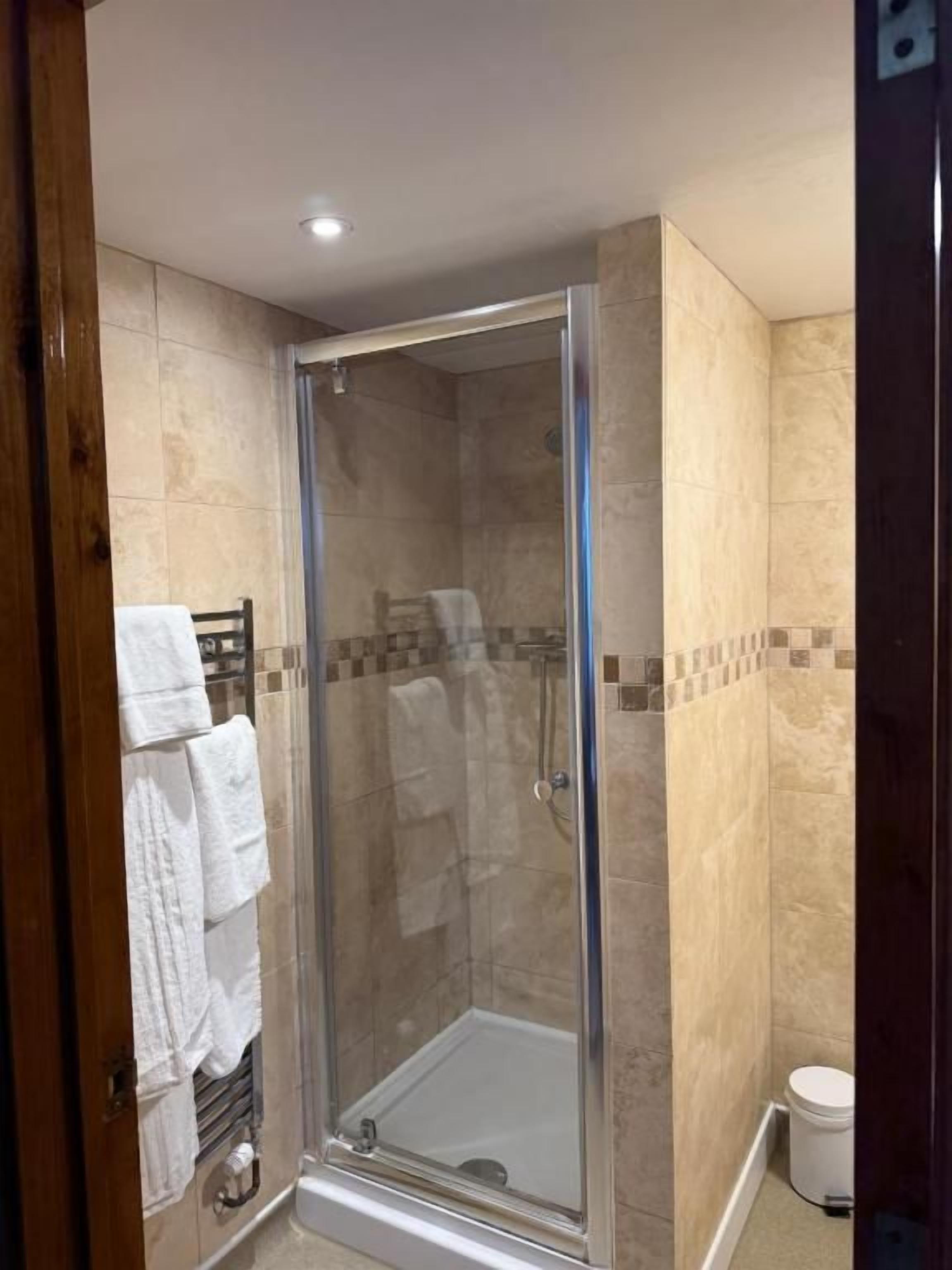A glass-enclosed shower area with a tiled floor and walls, a white towel rack, and a white toilet.