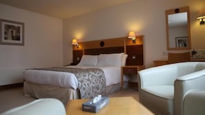 Una habitación de hotel con una cama, mesitas de noche, una silla, una pequeña mesa con una caja de pañuelos y un espejo en la pared.