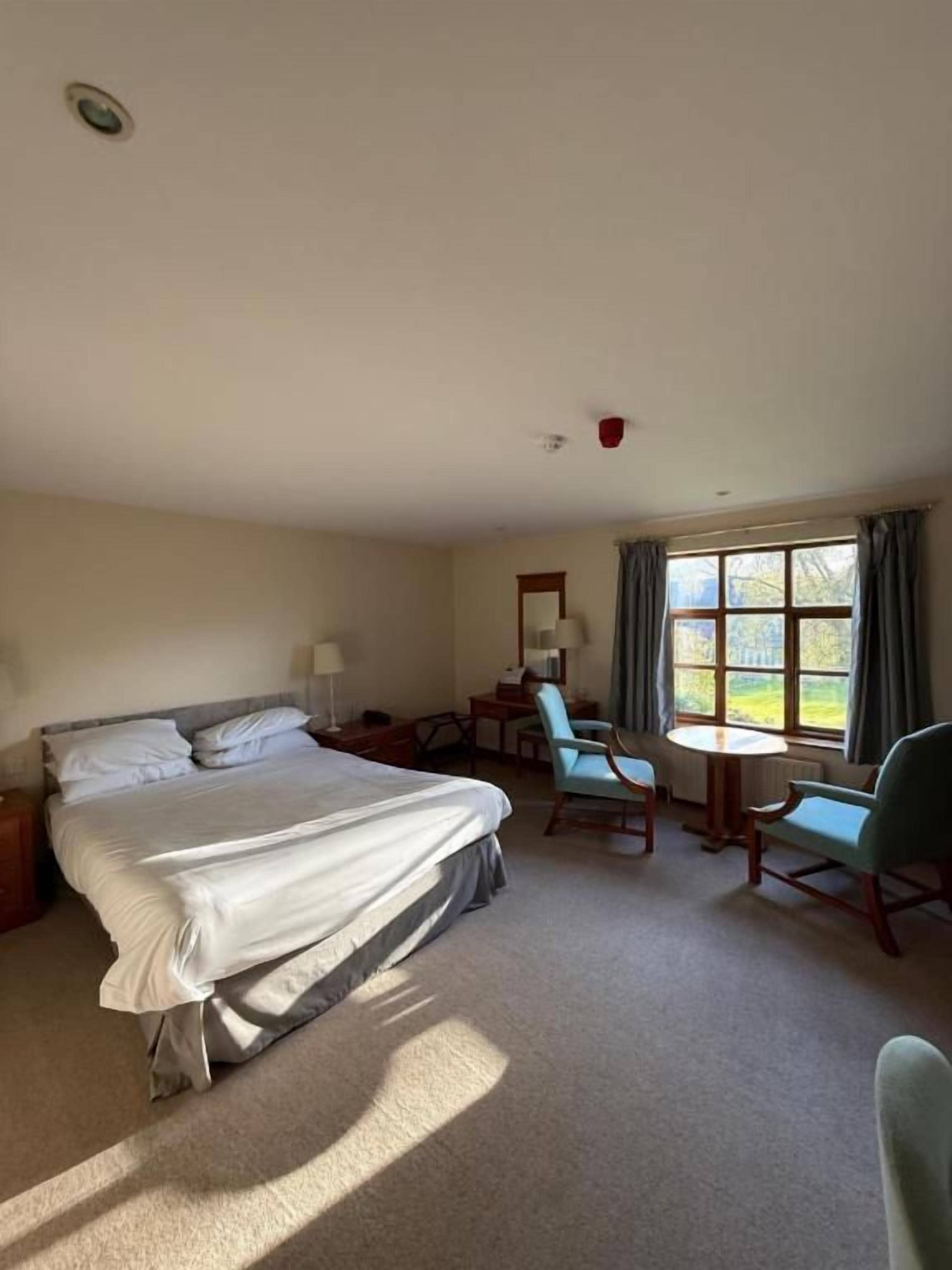 A hotel room with a bed, a desk, two chairs, a small table, and a window with curtains.