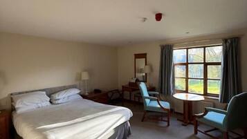 A hotel room with a bed, a desk, two chairs, a small table, and a window with curtains.