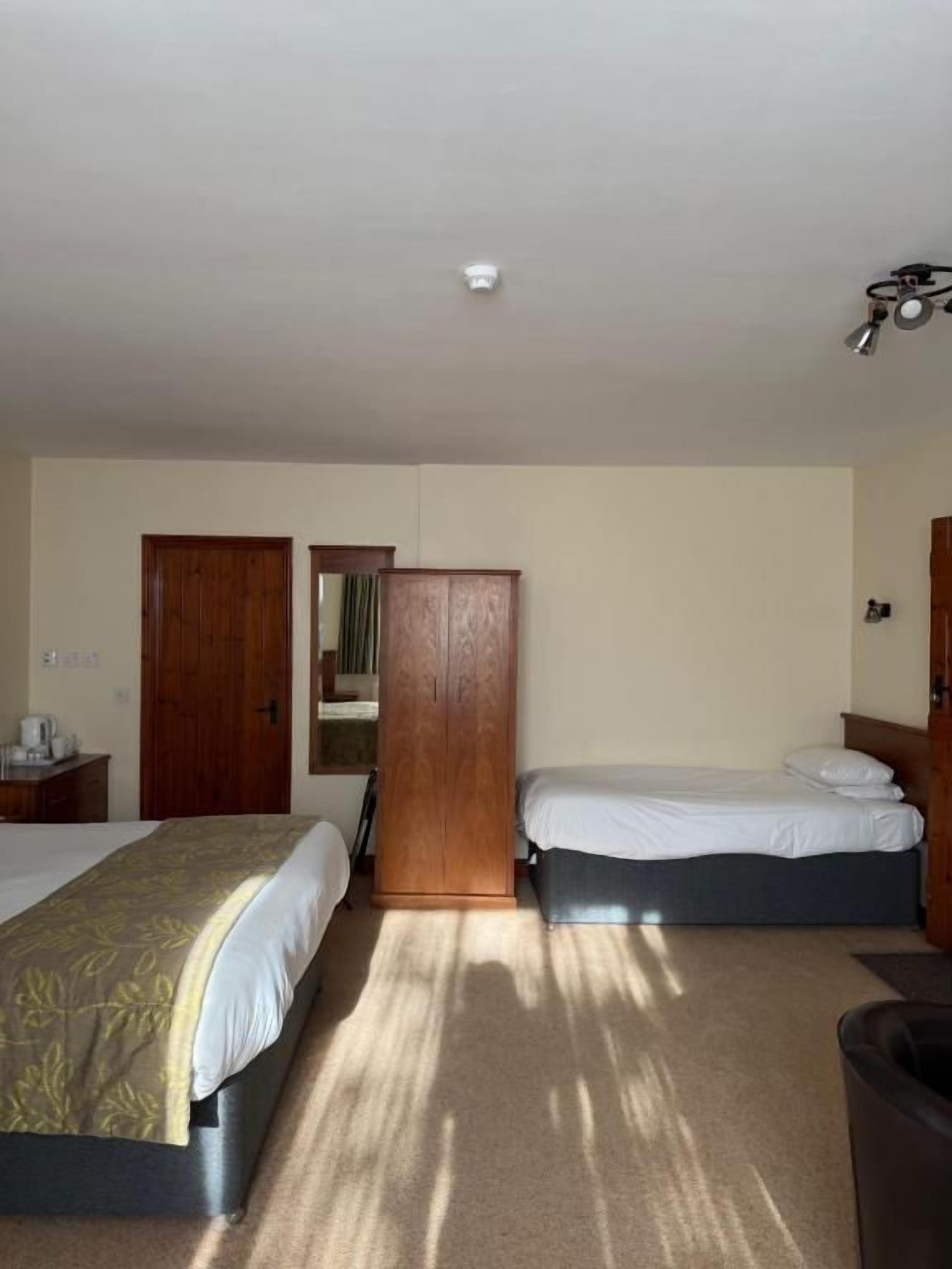 Habitación de hotel con dos camas, un armario, un escritorio y un cubo de basura.