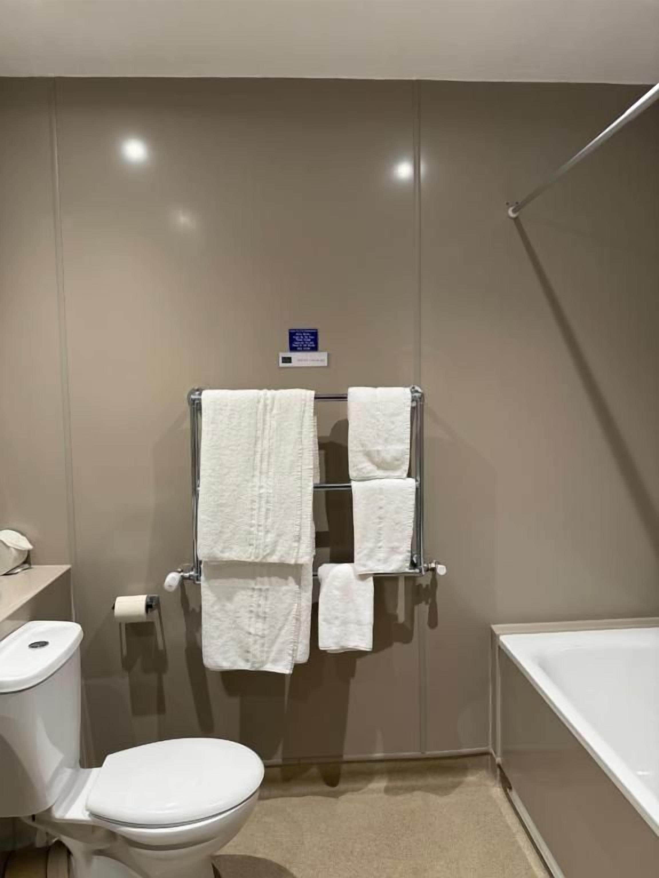A bathroom with a toilet, a towel rack with multiple towels, a shower area, and a bathtub.