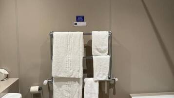A bathroom with a toilet, a towel rack with multiple towels, a shower area, and a bathtub.