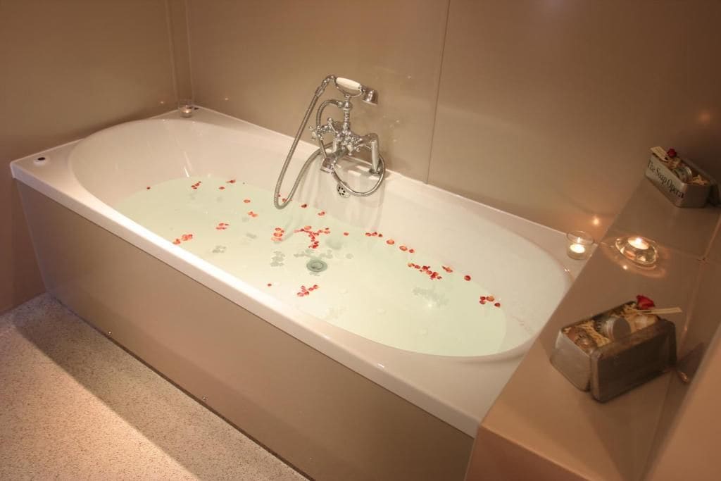 A bathtub with rose petals, a handheld showerhead, and candles.