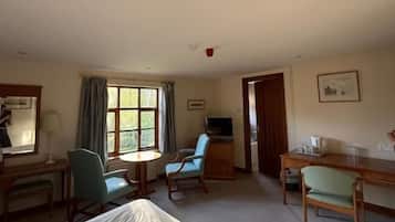 Habitación de hotel con cama, escritorio, silla, mesita, televisión y ventana con cortinas.