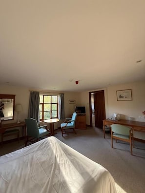 A hotel room with a bed, a desk, a chair, a small table, a television, and a window with curtains. - Ivy House Country Hotel (Lowestoft)