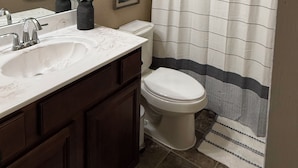 Un baño con lavamanos blanco, armarios de madera oscura, inodoro blanco y cortina de ducha a rayas.