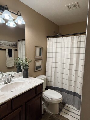 A bathroom with a white sink, dark wooden cabinets, a white toilet, and a shower curtain with a striped pattern. - Wonderful 3-bedroom house with AC in peaceful Morrilton (Morrilton)