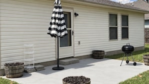 Una casa residencial con un patio techado, una parrilla y un paraguas a rayas.