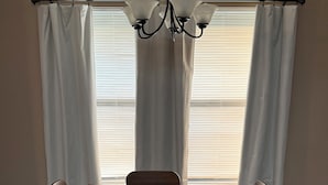 Un comedor con una mesa, cuatro sillas, una araña y una ventana con persianas.